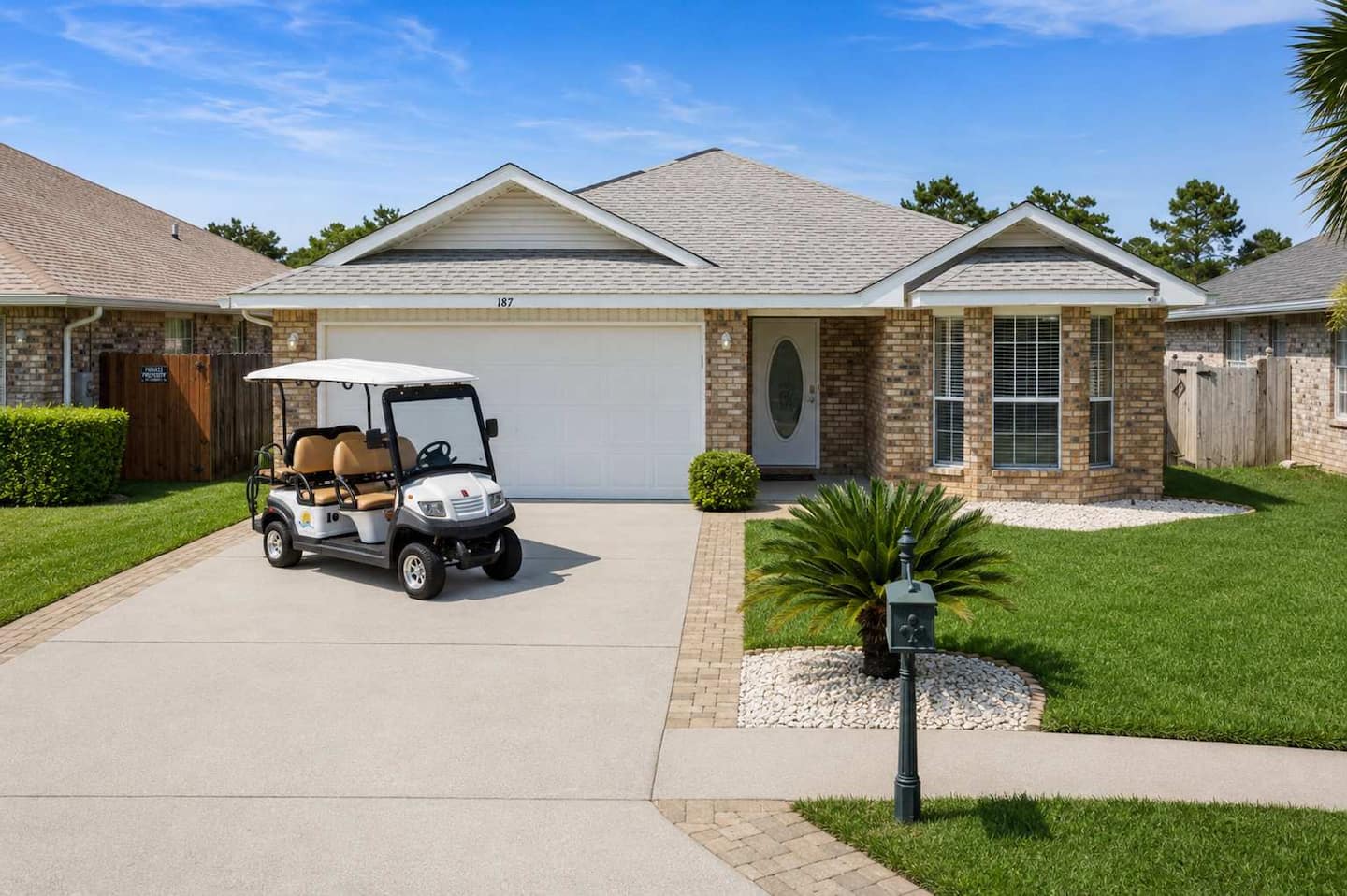 A charming brick home with a golf cart parked in the driveway, surrounded by lush green grass and landscaping.