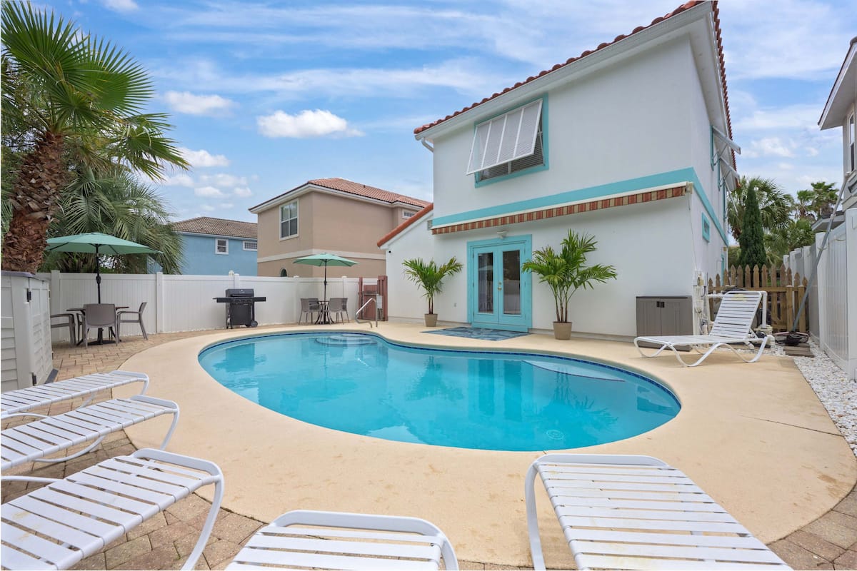 Bright vacation rental featuring a private pool, lounge chairs, and outdoor seating surrounded by palm trees.