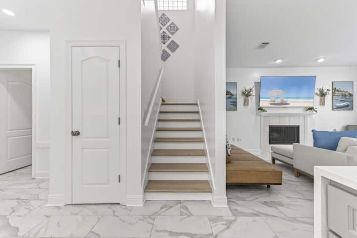 Bright, modern entryway featuring a staircase, marble flooring, and a cozy living area with artwork and a fireplace.