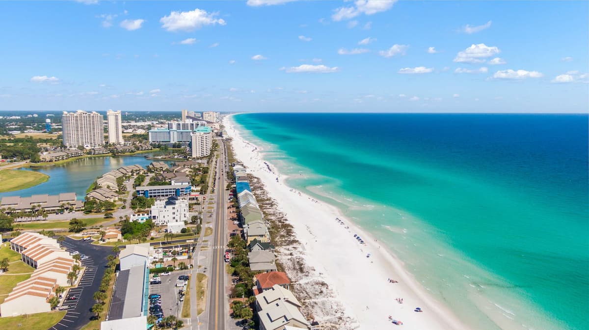 Vibrant turquoise waters meet a sandy beach lined with umbrellas under a clear blue sky, inviting relaxation and leisure.