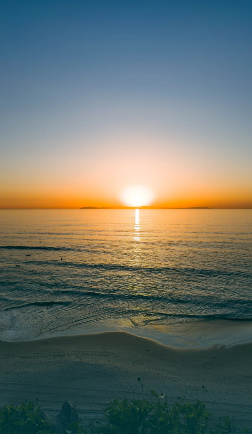Sunset over calm ocean with sandy shore.