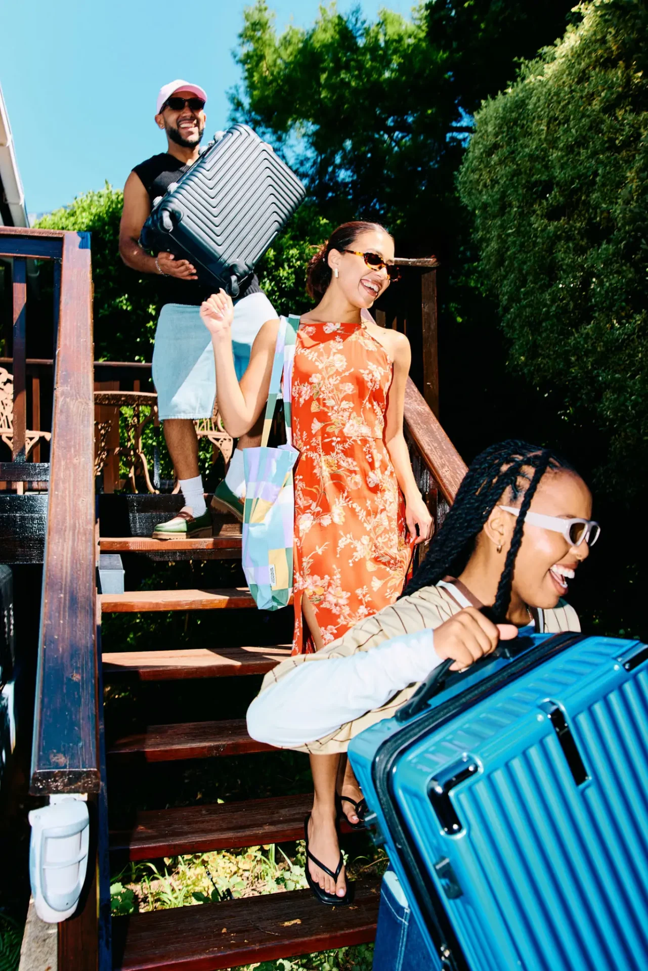 Three friends carrying suitcases down stairs