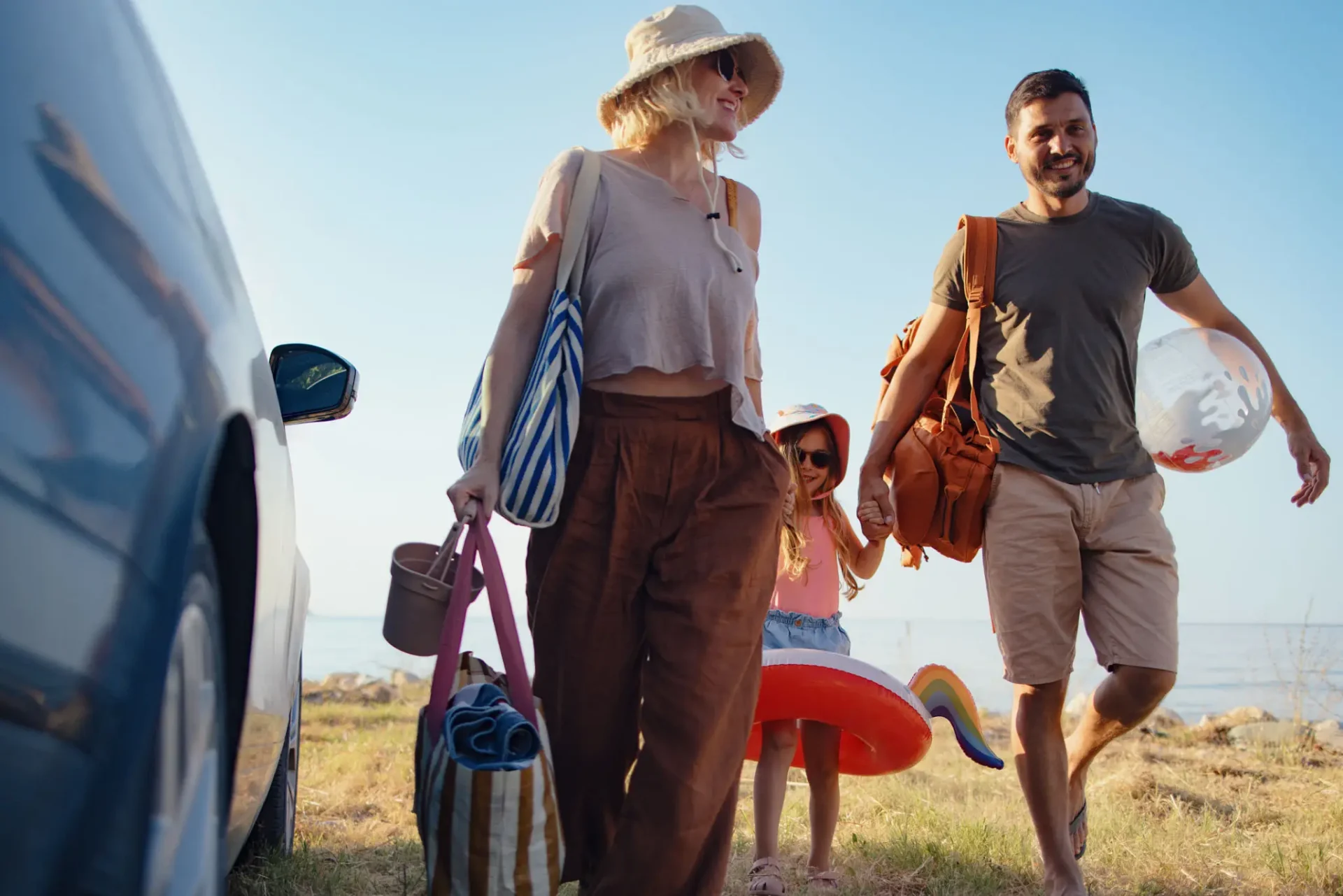 Family carrying beach gear walking by car