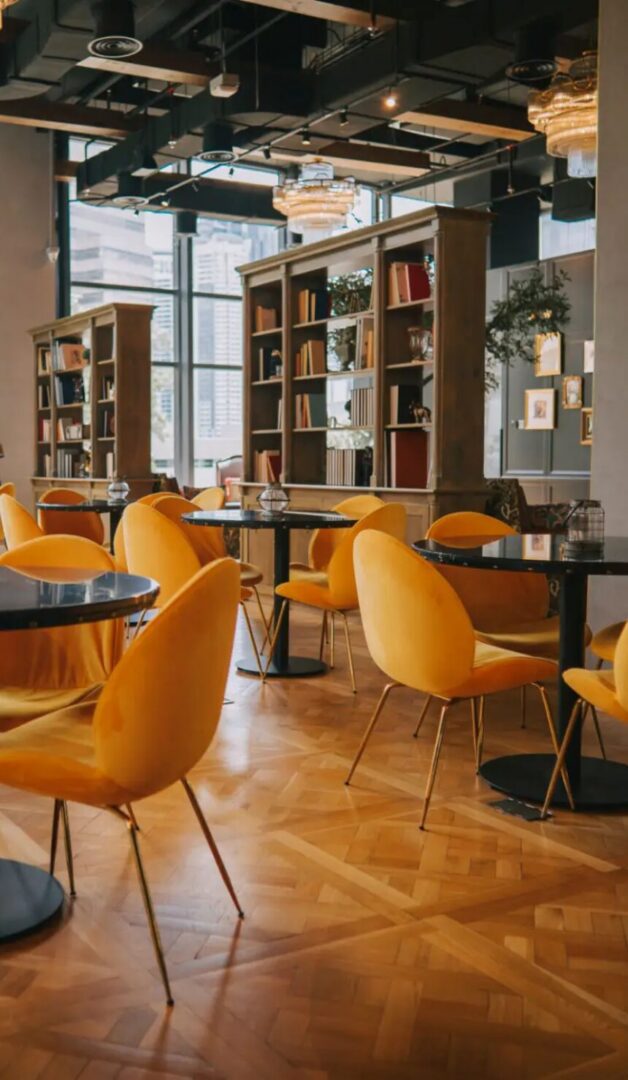 Stylish café interior featuring yellow chairs, black tables, and bookshelves, creating a cozy atmosphere for visitors.